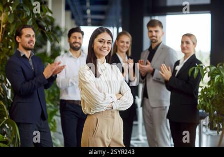 Glückliche, selbstbewusste junge Frau, die in die Kamera blickt und im modernen Büro lächelt. Stockfoto