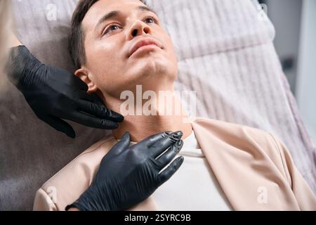 Kosmetologische Frau in Gummihandschuhen, die männlichen Klientelhals untersucht Stockfoto