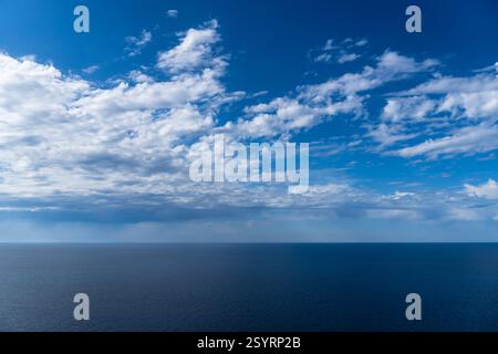 Der weite Ozean erstreckt sich bis zum Horizont unter einem ruhigen Himmel voller weicher, flauschiger Wolken, die ein Gefühl von Frieden und Ruhe schaffen. Stockfoto