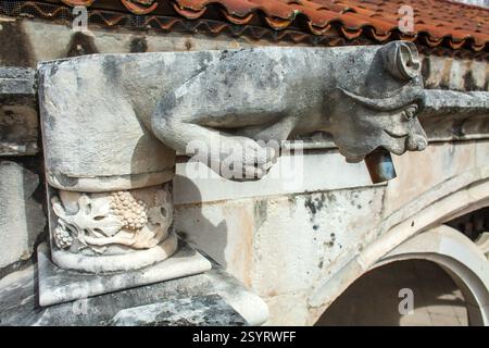 Ein grotesker Gargoyle aus Stein, der als Wasserauslauf auf einem historischen Gebäude dient und die komplizierten Details und skurrilen Elemente hervorhebt Stockfoto