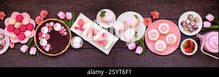 Mothers Day Tischszene mit einer Auswahl an Desserts und Süßigkeiten. Oben auf einem dunklen Holzbanner Hintergrund. Rosafarbenes Blumenmotiv. Stockfoto