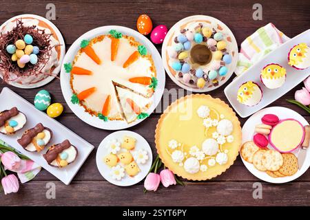 Ostern oder Frühling Dessert Esstisch Tisch Szene. Blick von oben über dunklem Holzhintergrund. Zitronentorte, Cupcakes, Osterei und Karottenkuchen und eine Auswahl Stockfoto