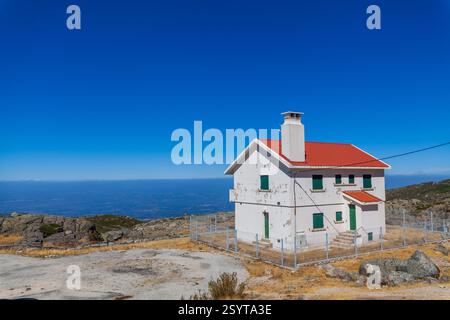 Ein weißes Haus mit einem roten Dach befindet sich auf einem felsigen Berg mit Blick auf eine weite Landschaft unter einem klaren blauen Himmel Stockfoto