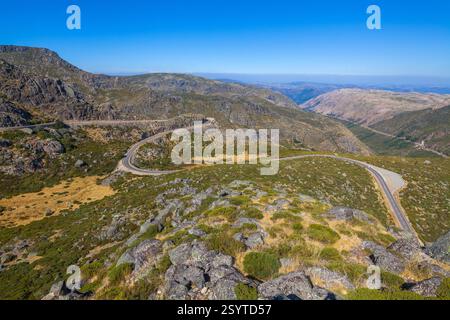 Eine gewundene Straße schlängelt sich durch eine bergige Landschaft mit karger Vegetation unter einem klaren blauen Himmel und zeigt einen malerischen Bergpass Stockfoto