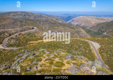 Eine gewundene Straße schlängelt sich durch eine bergige Landschaft mit karger Vegetation unter einem klaren blauen Himmel und zeigt einen malerischen Bergpass Stockfoto