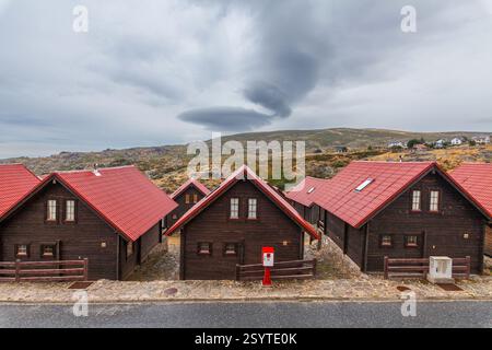 Eine Reihe von Holzhütten mit roten Dächern steht vor einem Hintergrund von Hügeln und einem dramatischen bewölkten Himmel Stockfoto