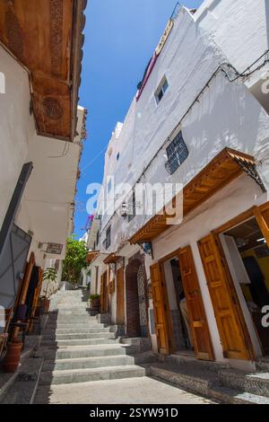 Enge Straße mit weiß getünchten Gebäuden, Holztüren und Rollläden und einer Treppe, die unter einem klaren blauen Himmel nach oben führt, schafft ein malerisches Ich Stockfoto