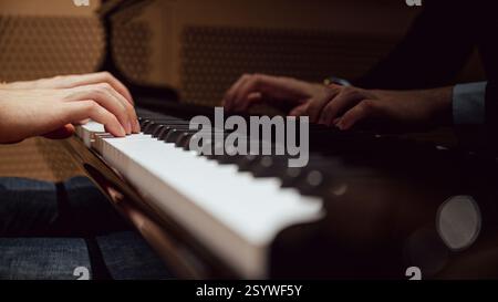 Eine Nahaufnahme der Hände eines Pianisten, die anmutig ein Klavier spielen, mit einer warmen Reflexion auf der glänzenden Oberfläche, die eine intime und künstlerische Atmosphäre schafft. Stockfoto
