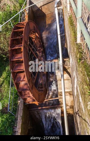 Ein rostiges Wasserrad mit fließendem Wasser, Teil eines kleinen Damms oder Bewässerungssystems Stockfoto
