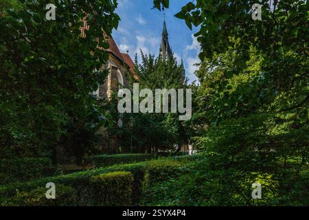 Eine malerische Szene eines historischen Gebäudes mit einem hohen Turm und einem roten Dach, teilweise von üppigen grünen Bäumen und Laub verdeckt, gesehen an einem hellen Tag wi Stockfoto