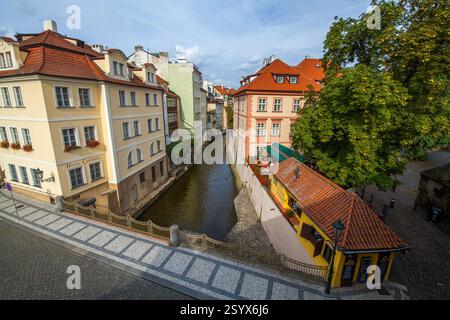 Ein schmaler Kanal, der von farbenfrohen Gebäuden mit roten Ziegeldächern gesäumt ist, mit einer kleinen Brücke und einem Hotelschild, unter einem bewölkten Himmel mit einem Baum im Vordergrund Stockfoto
