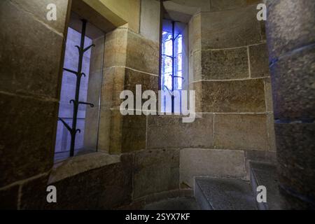 Eine Nahaufnahme einer Wendeltreppe aus Stein mit zwei kleinen Fenstern, eines zeigt einen Blick auf blaues Glas. Stockfoto