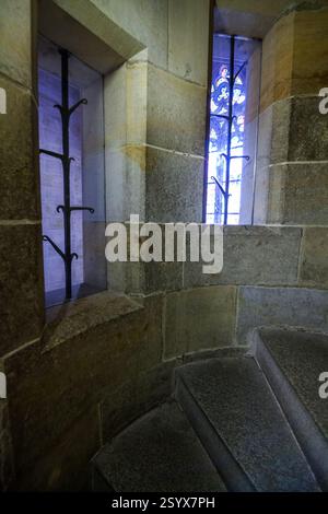 Eine Nahaufnahme einer Wendeltreppe aus Stein mit zwei kleinen Fenstern, eines zeigt einen Blick auf blaues Glas. Stockfoto