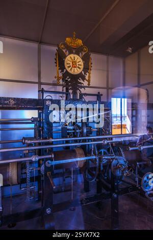 Ein komplexer Uhrwerkmechanismus mit Zahnrädern, Rädern und einem großen Zifferblatt mit römischen Ziffern, das in einem Glasgehäuse dargestellt wird und die Int. Stockfoto