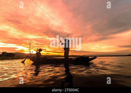 Silhouette Fischer fischen mit Netz auf dem Boot in Morgen in Thailand, Natur und Kultur Konzept Stockfoto