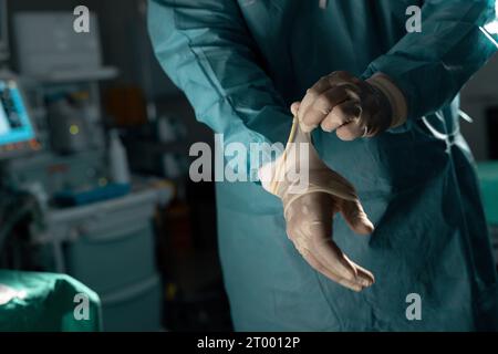 Mittelschnitt eines birassischen männlichen Chirurgen mit Operationskittel und Handschuhen im Operationssaal Stockfoto