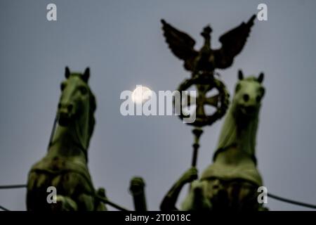 Berlin, Deutschland. Oktober 2023. Der Mond untergeht am frühen Morgen zum Jahrestag der Wiedervereinigung der beiden deutschen länder am 3. Oktober 1990 hinter dem Brandenburger Tor. Quelle: Fabian Sommer/dpa/Alamy Live News Stockfoto