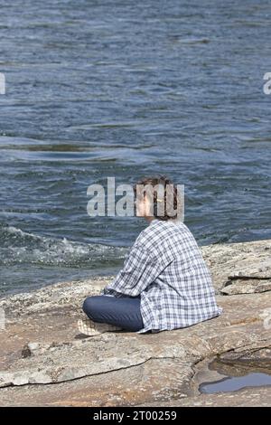 Die junge Frau hört Musik am Fluss. Stockfoto