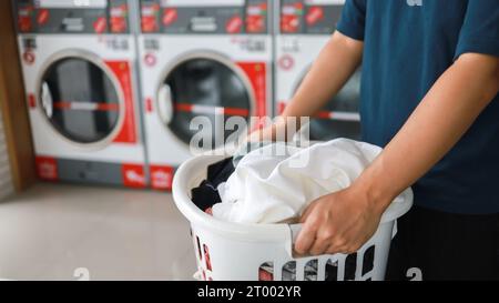 Hausmann mit Korb und schmutziger laundryÂ gewaschener Kleidung im Waschraum. Waschen machineÂ im Wäschereigeschäft Stockfoto