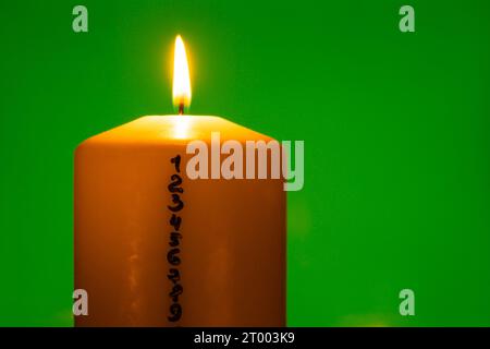 Kerze mit Adventskalender auf grünem Chroma-Hintergrund traditionelle brennende Wachskerzen mit Zahlen, die für Weihnachten herunterzählen. Wunderschönes Advent Zu Hause. Festliche Kerzenleuchtung Und Dunkler Hintergrund. Heiligabend Stockfoto