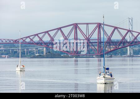 Zwei Yachten, die den Firth of Forth hinaufsegeln, mit der Forth Bridge im Hintergrund. Stockfoto