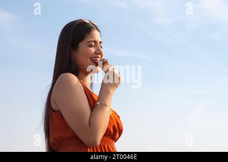 Porträt einer jungen Frau, die Eis im Kegel vor blauem Himmel isst Stockfoto