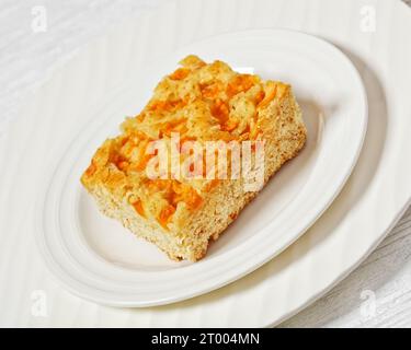 Pfirsichkuchen quadratische Scheibe auf weißem Teller auf weißem Holztisch, horizontale Ansicht, Nahaufnahme Stockfoto
