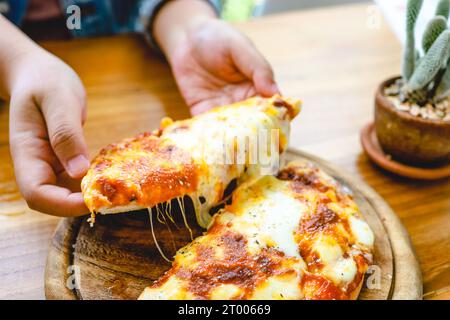 Eine Scheibe frischer, heißer, sehr käsiger vegetarischer Pizza, Mozzarella. Italienische Pizza Margherita in der Hand Stockfoto