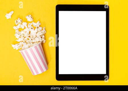 Leeres Tablet mit weißem Bildschirm und Popcorn-Eimer auf gelbem Hintergrund. Vorlagenmodell. Draufsicht Stockfoto