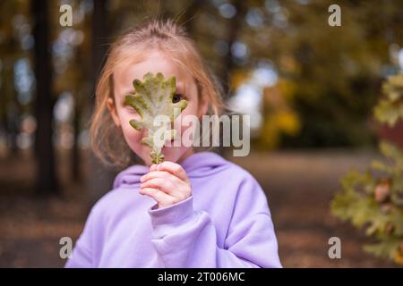 Glückliches kleines Mädchen sammelt und spielt mit herbstlich gefallenen Blättern im Herbstpark. Herbstsaison Stockfoto