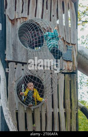 Ein Kind klettert an einem heißen Sommertag in einem Park auf einem Spielplatz auf ein alpines Gitter. Kinderspielplatz in einem öffentlichen Park, Entertai Stockfoto