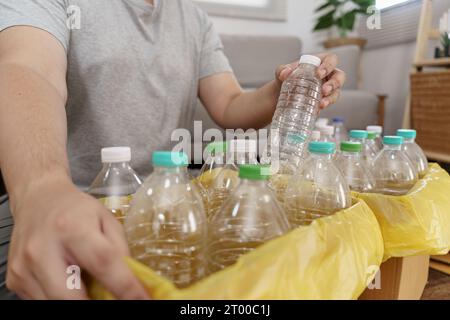 Recyceln Sie den umweltfreundlichen Zero Concept-Mann, der leere Plastikflasche in den Recyclingbehälter mit gelben Mülltüten zu Hause wirft Stockfoto