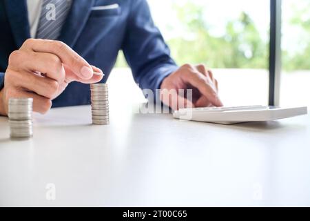 Geld sparen. Geschäftsmann Buchhalter verifizieren wachsende Geschäfte und sparen Geld beim Stapeln von Münzen mit Taschenrechner. Buchhaltung Stockfoto