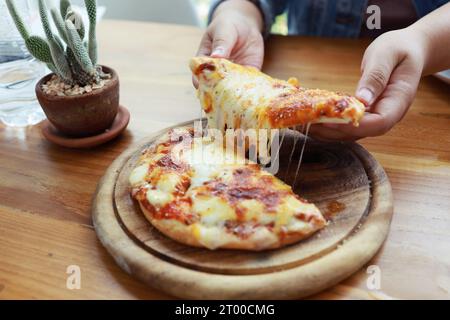 Eine Scheibe frischer, heißer, sehr käsiger vegetarischer Pizza, Mozzarella. Italienische Pizza Margherita in der Hand Stockfoto