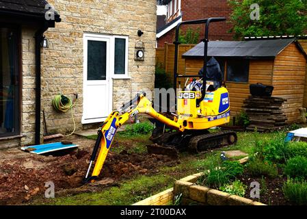 Minibagger in einem Garten, der zum Ausgraben von Boden für den Bau eines Wintergartens verwendet wird, Chard, Somerset, Großbritannien, Europa. Stockfoto