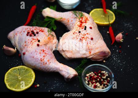 Rohe Hähnchenschenkel, Knoblauch, Chili, Zitrone und Kräuter auf schwarzem Hintergrund. Stockfoto
