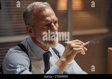 Ambient-Porträt eines gutaussehenden leitenden Detektivs, der den Fall im Büro und Rauchen studiert Stockfoto