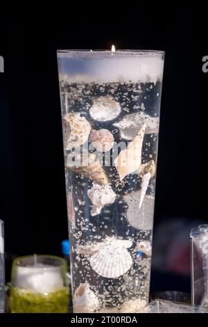 Transparente brennende Kerze mit Muscheln und Schnecken, die in das transparente Kerzenwachs eingearbeitet sind, mit sehr nautischem Flair Stockfoto