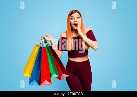 Der Black friday wunderte sich über eine junge Frau mit überraschtem Gesicht, die seine Hand nahe der Wange hält, mit weit offenen Augen und Mund in der anderen Hand, die Einkäufe hält Stockfoto