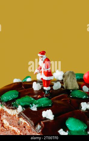 Ein miniatursanta claus steht neben einem Sack mit Geschenken, auf einem Baumkuchen, vor einem gelben Hintergrund mit etwas leerem Platz oben Stockfoto