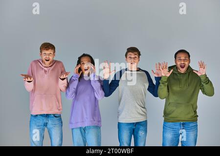 Vier schockierte multikulturelle Freunde in bunten Straßenbekleidung vor grauem Hintergrund, kulturelle Vielfalt Stockfoto