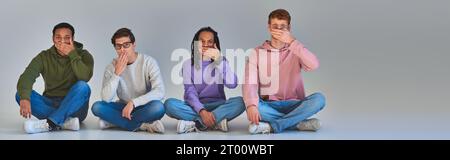 Vier junge Freunde sitzen mit überkreuzten Beinen und bedecken den Mund, kulturelle Vielfalt, Banner Stockfoto