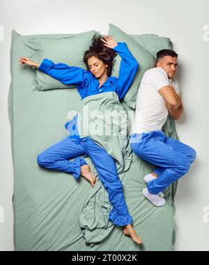 Junge, schöne Frau, bedeckt mit Decke über dem Bett und Mann, der auf der Seite lag und eiskalt im Pyjama trug, Paar, das sich in einem großen Minzbett entspannte. Stockfoto