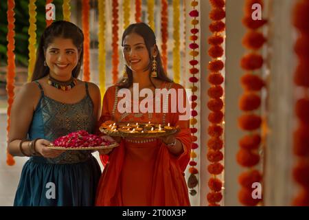 Porträt zweier glücklicher Schwestern, die Lampen und Rosenblätter auf Diwali halten Stockfoto
