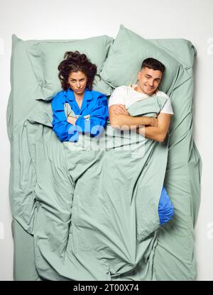 Junge schöne Frau und attraktiver Mann, der auf dem Rücken lag, kreuzten die Hände auf der Brust, Paare, die sich in einem großen Minzbett entspannen. Schlechter Morgen. Stockfoto