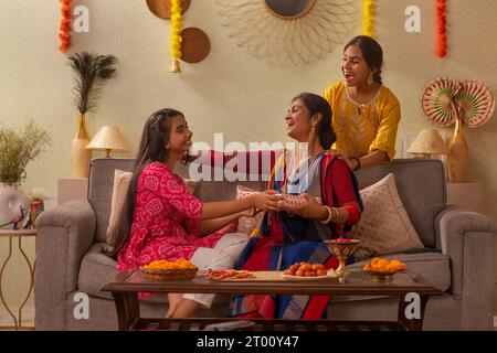 Die bengalische Familie tauscht anlässlich der Durga Puja zusammen auf dem Sofa im Wohnzimmer ein Geschenk aus Stockfoto