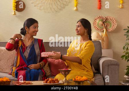 Die bengalische Familie tauscht anlässlich der Durga Puja zusammen auf dem Sofa im Wohnzimmer ein Geschenk aus Stockfoto