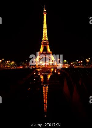 Beleuchteter Eiffelturm bei Nacht, der seine majestätische Reflexion im ruhigen Vordergrundteich zeigt Stockfoto
