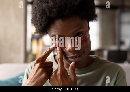 Porträt eines afroamerikanischen Mannes, der zu Hause auf der Couch sitzt und unter Augenmasken aufträgt Stockfoto