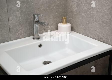Modernes Waschbecken. Stilvolles weißes Waschbecken mit Wasserhähnen in moderner Einrichtung. Wasserhahn aus Chrommaterial. Haushaltsgeräte. Graues Badezimmer. Haushaltsgeräte Stockfoto